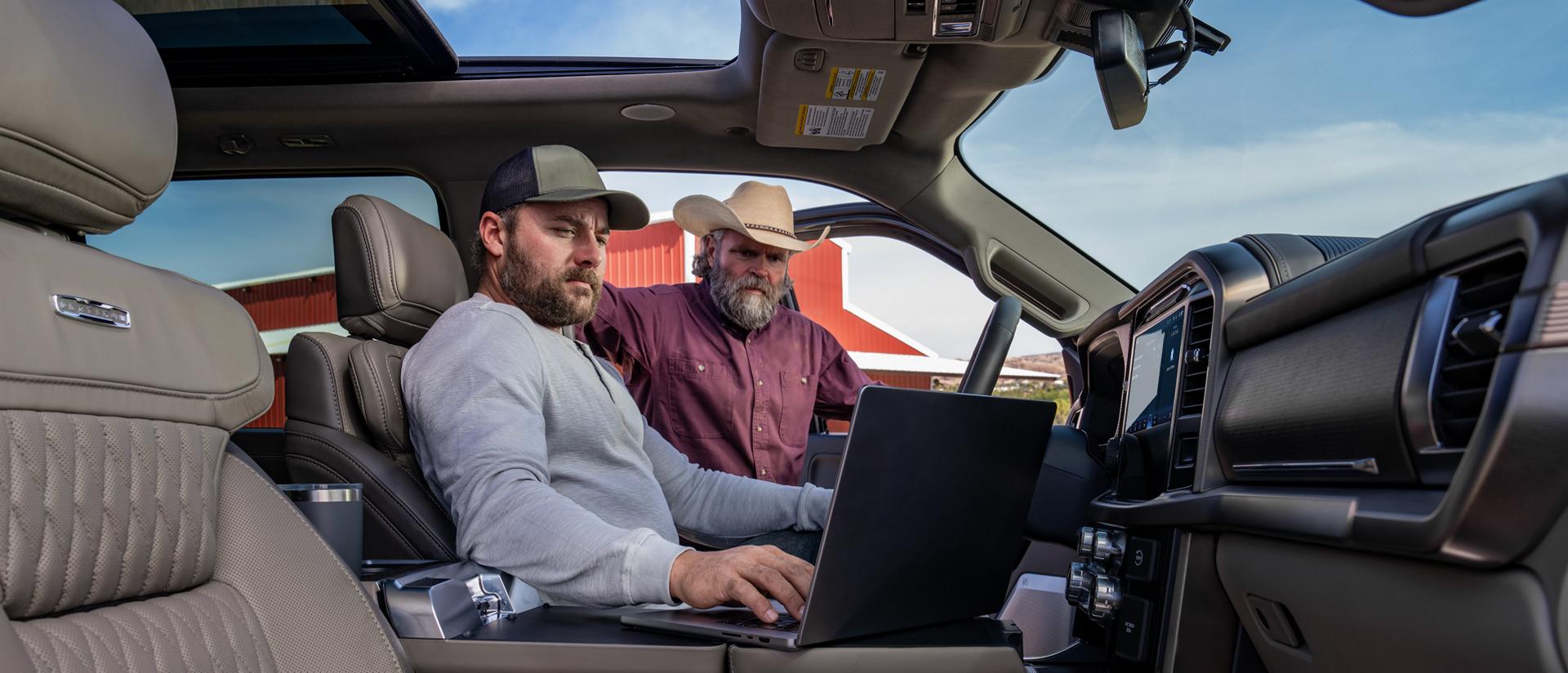 Person working on a laptop computer using the Interior Work Surface while another person watches from outside the cab 