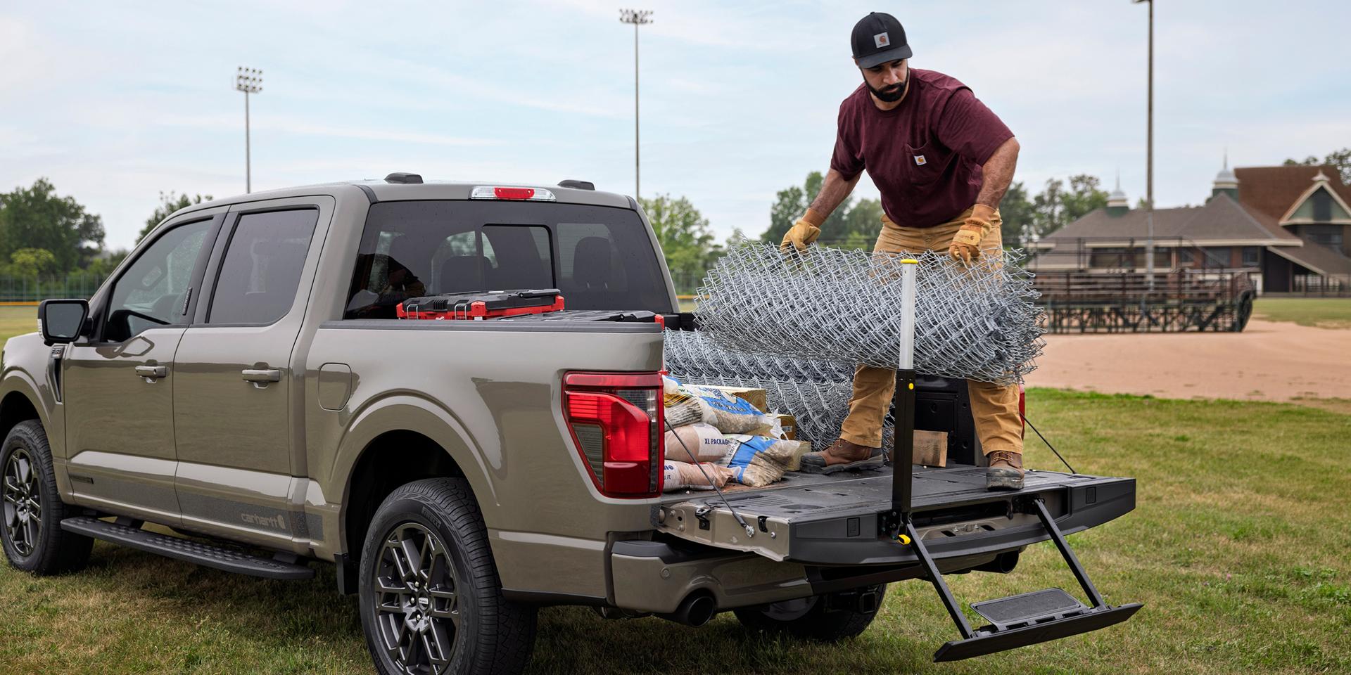 Man loading fencing into the bed of a 2027 Ford F-150® XLT model with the Carhartt® Package showing the tailgate step