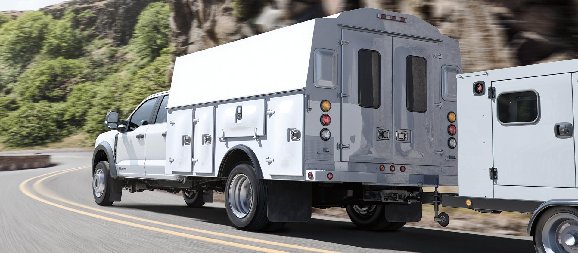 A 2026 Ford Super Duty® Chassis Cab with a utility box being driven up a road alongside a mountain