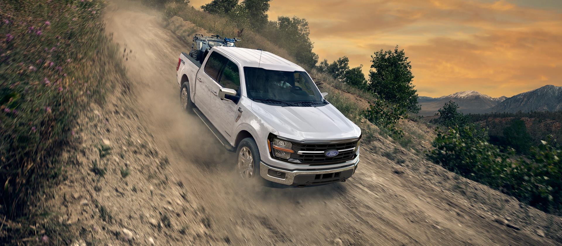 2026 Ford F-150® XLT model in Oxford White being driven down a dirt road with an ATV in the bed