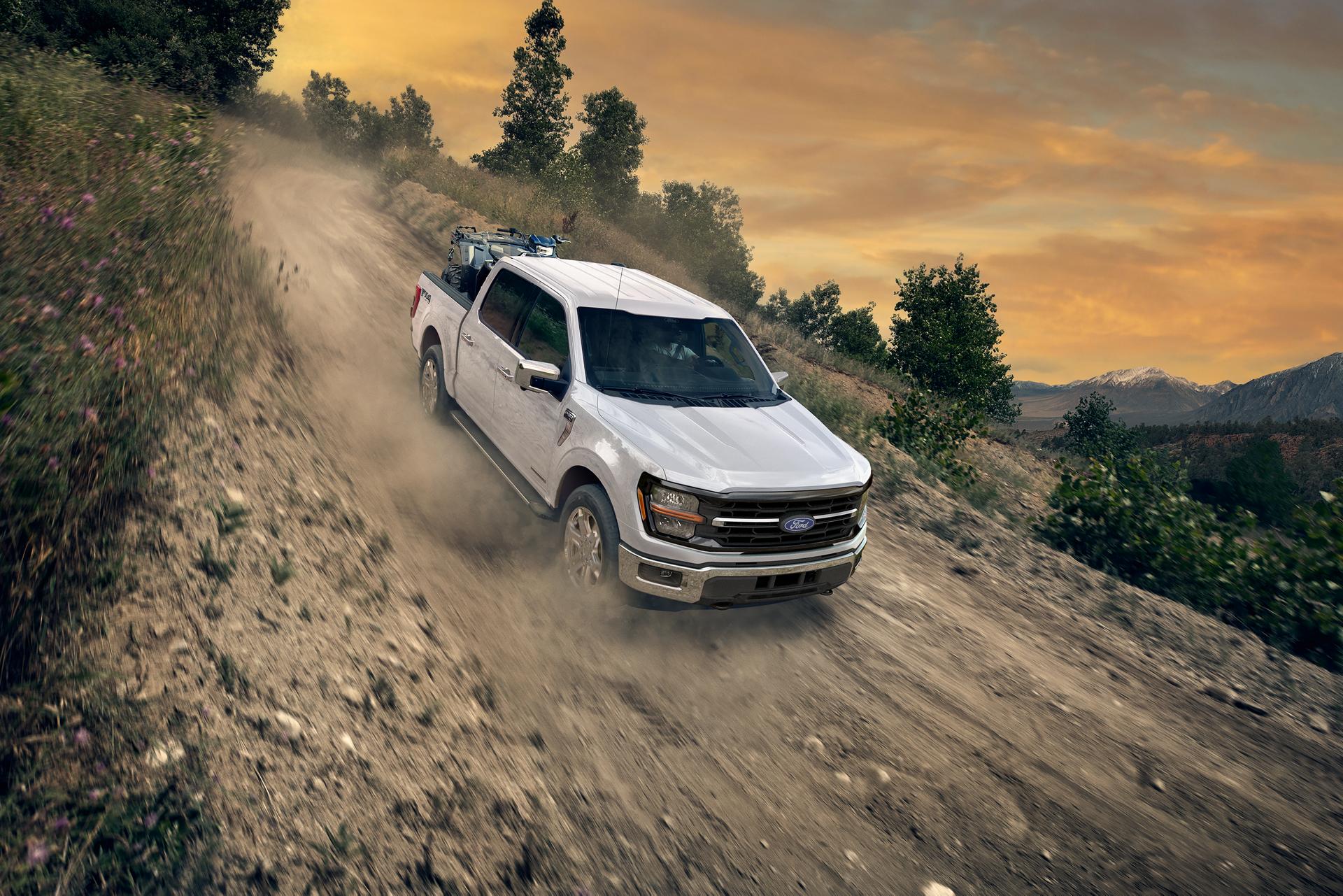 2026 Ford F-150® XLT model in Oxford White being driven down a dirt road with an ATV in the bed