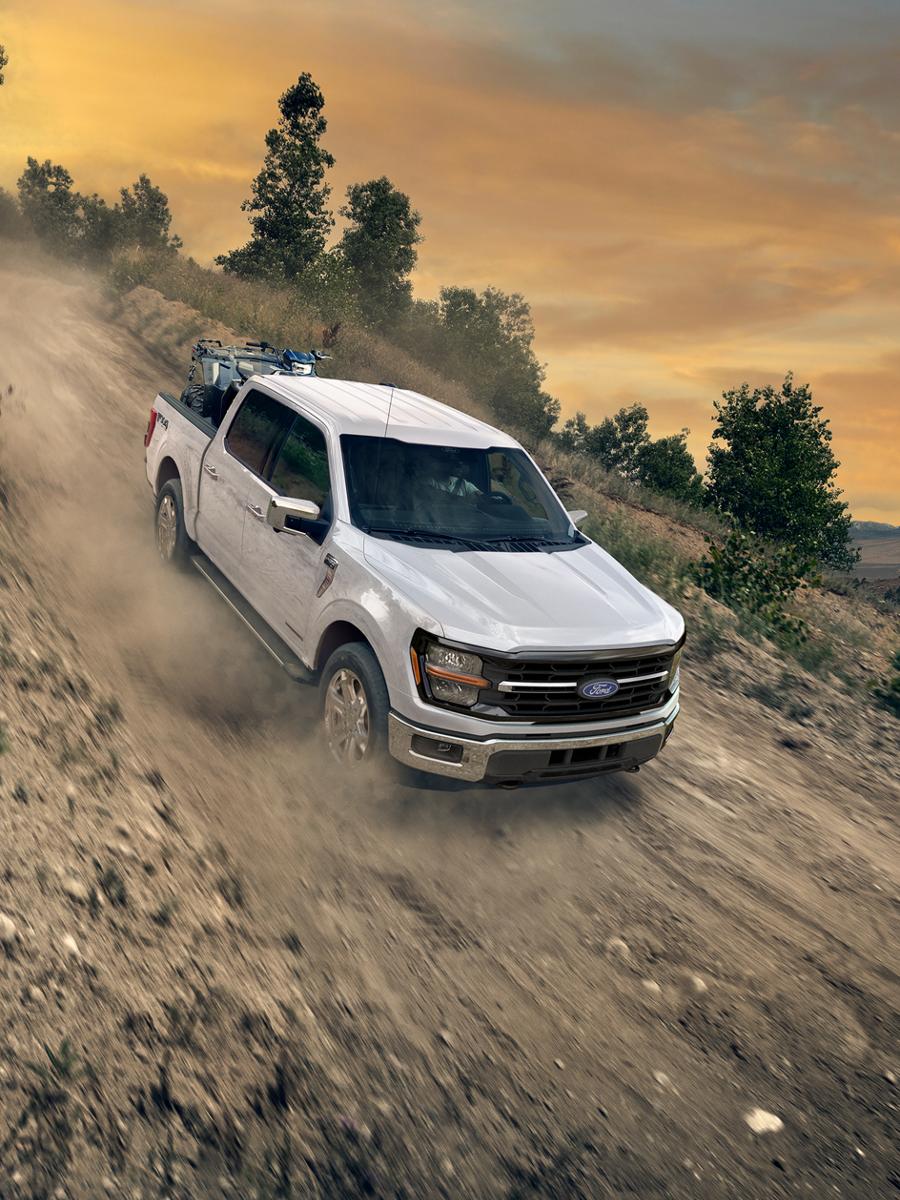 2026 Ford F-150® XLT pickup in Oxford White being driven down a dirt road with an ATV in the bed