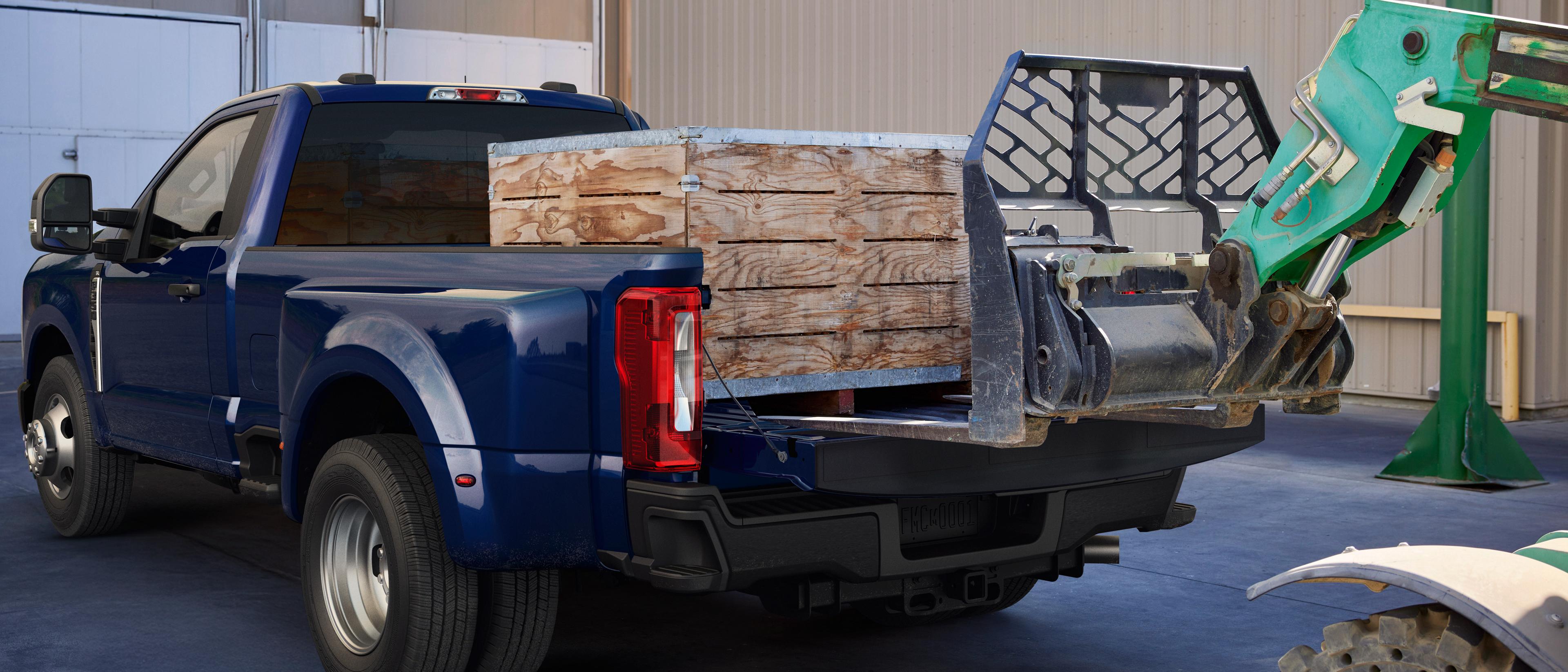 2026 Ford Super Duty® F-350® Lariat® pickup in Argon Blue with the tailgate open and operating a forklift