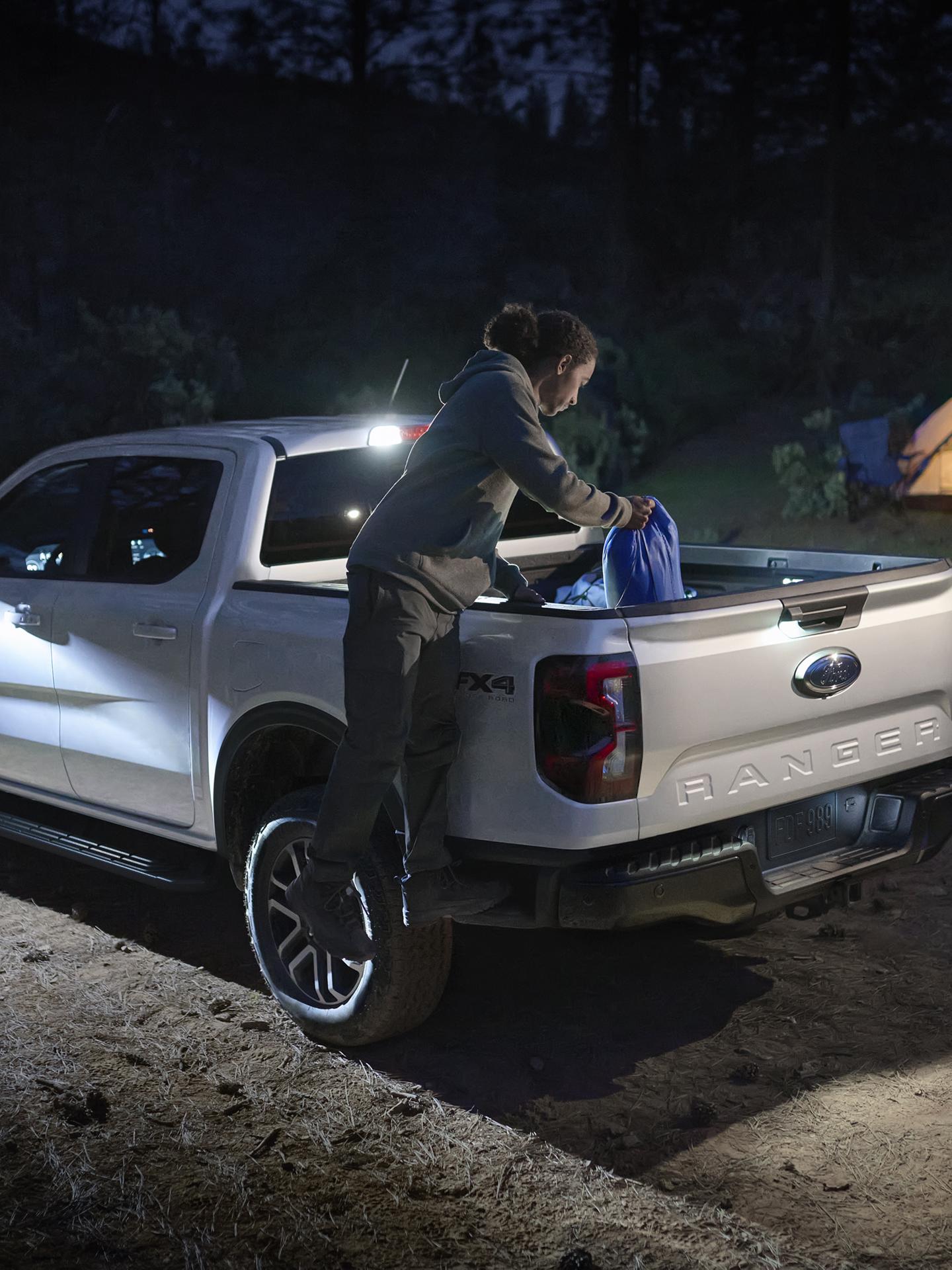 A person climbing into the bed of their 2026 Ford Ranger® Lariat® truck to grab a backpack
