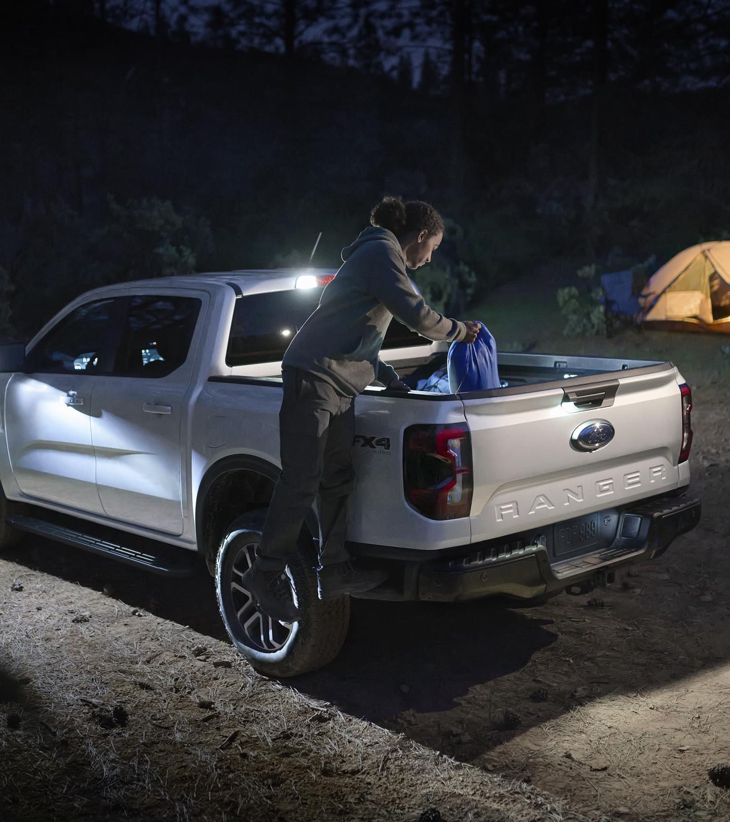 A person climbing into the bed of their 2026 Ford Ranger® Lariat® truck while using the Zone Lighting feature