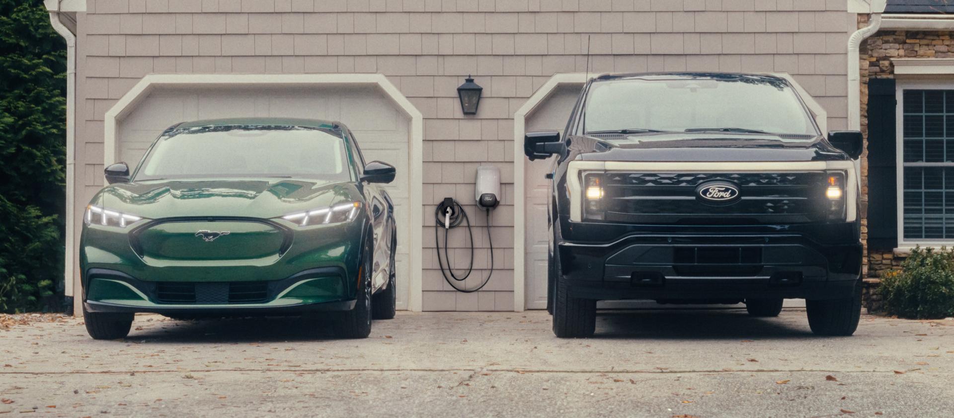 A Mustang Mach-E and F-150 Lightning parked in front of a house with a home charge station mounted on the garage.