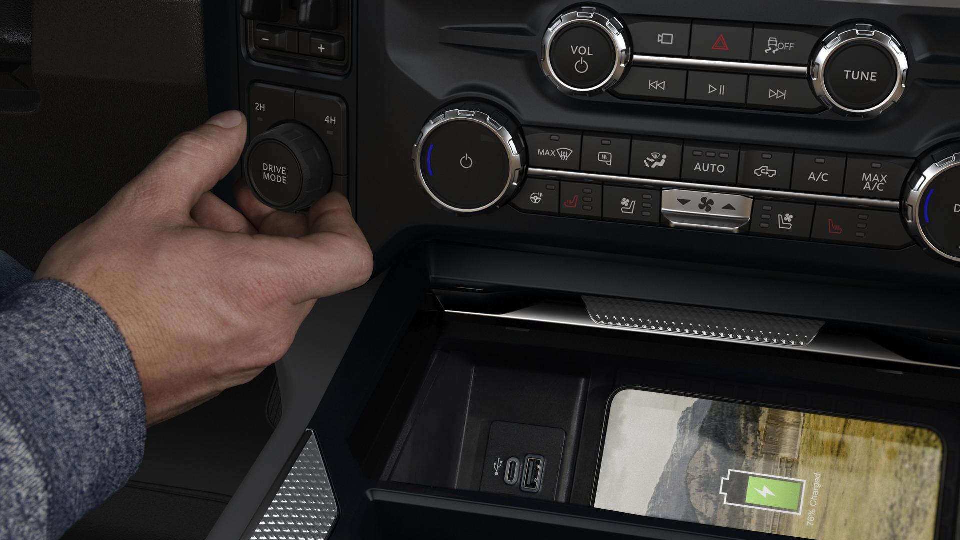 Adjusting the Drive Mode knob inside a 2026 Ford Super Duty®, while a phone charges with the wireless charging pad