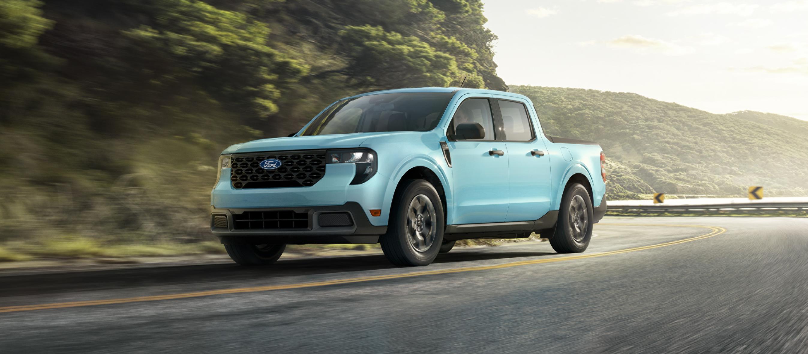 A 2026 Ford Maverick® pickup being driven on a winding road near a mountain lake