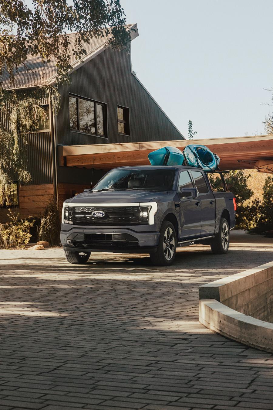 2026 Ford F-150® Lightning® pickup in Oxford White parked in a driveway with kayaks on a kayak rack in the bed